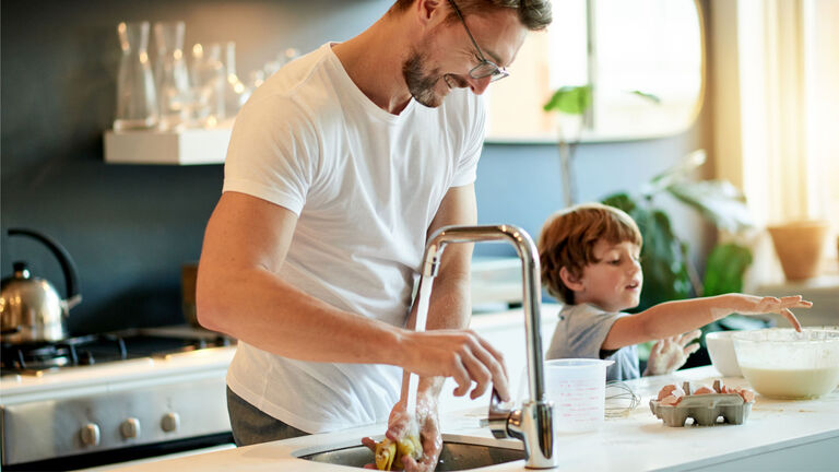 man washing dishes with child tasting batter